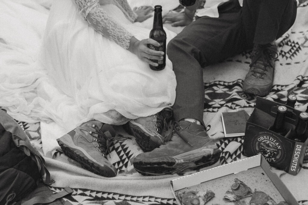 bride and groom in wedding attire and hiking boots enjoy pizza and beer at lakeside elopement
