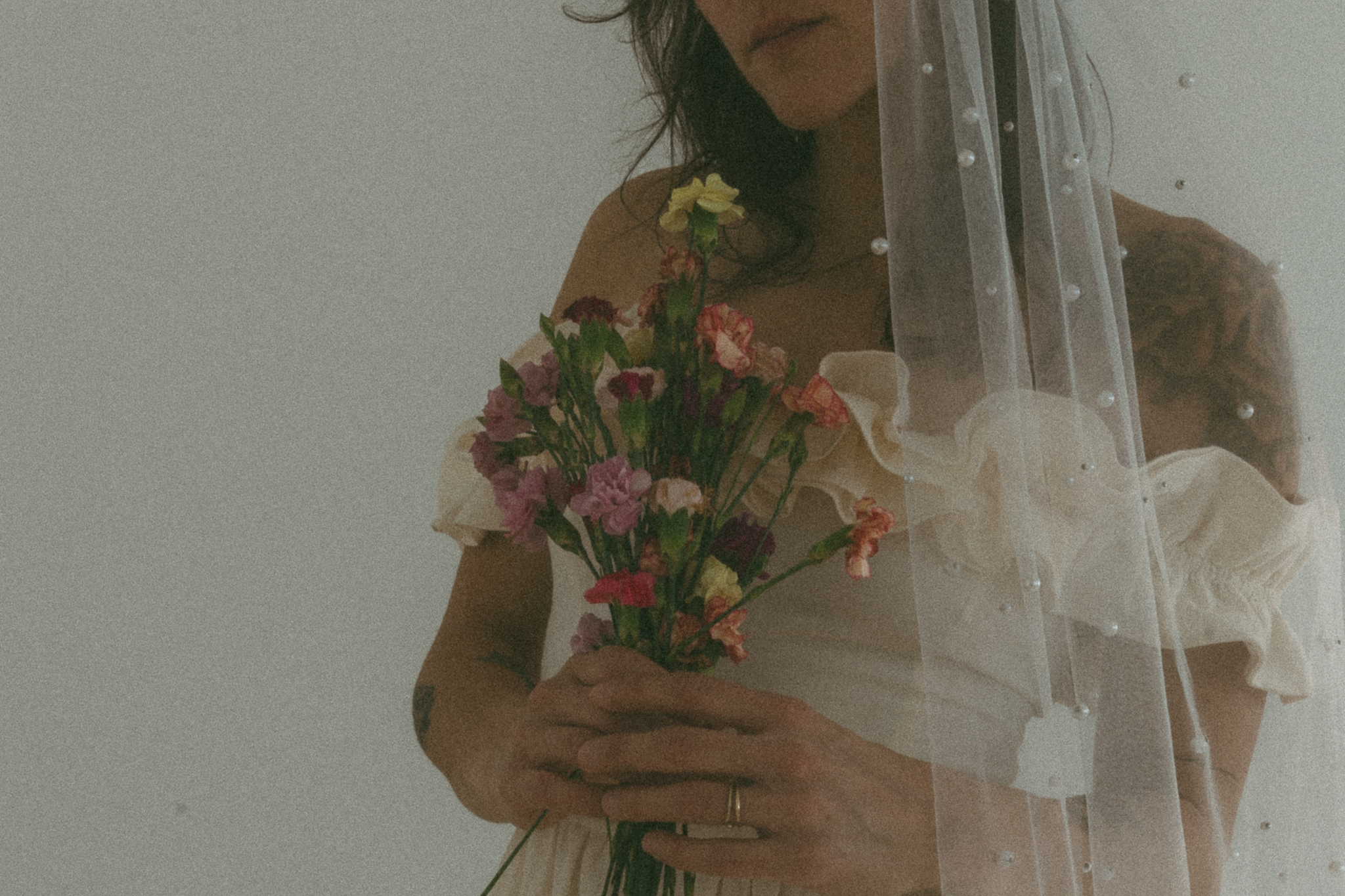 bride wearing a pearl veil holds flower bouquet while shooting in a studio