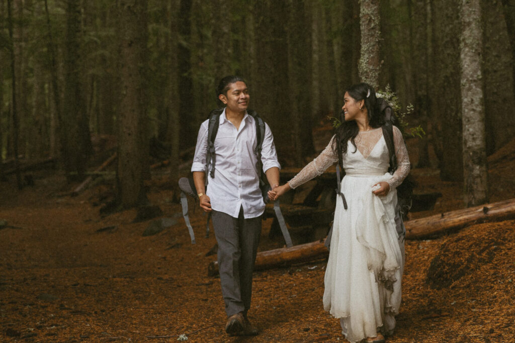 Bride and groom in their wedding attire hiking through a forest trail during their adventure elopement