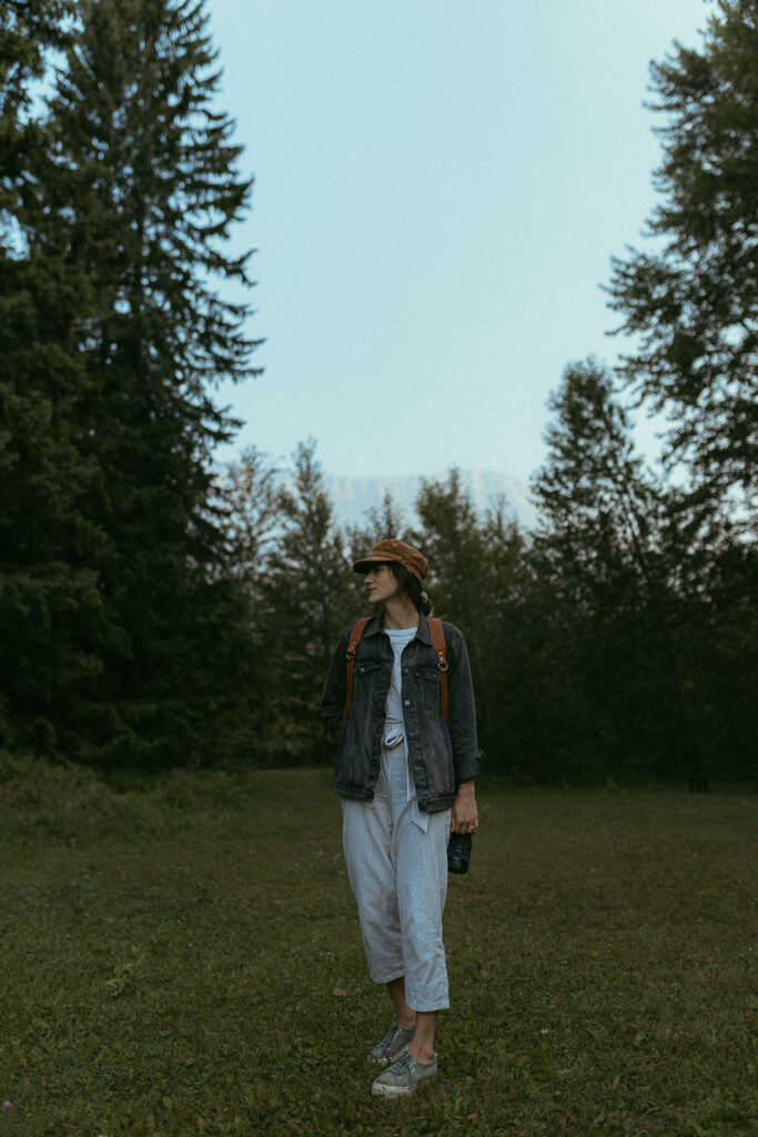 female photographer wearing a hat and camera harness in the forest
