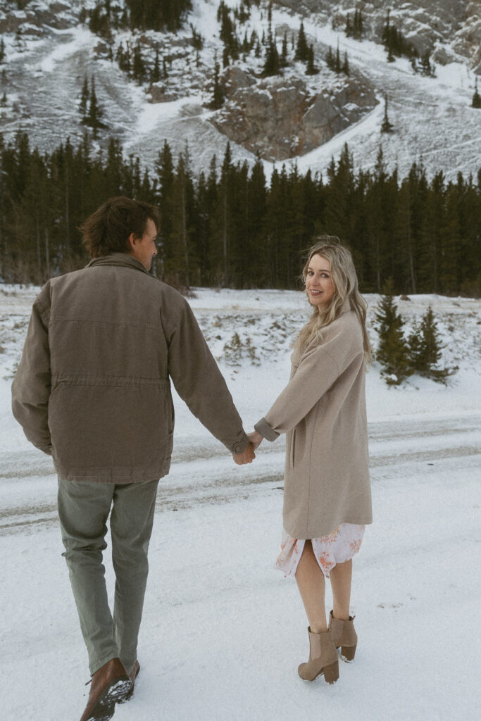 young couple holds hands while talking with a mountain in the background