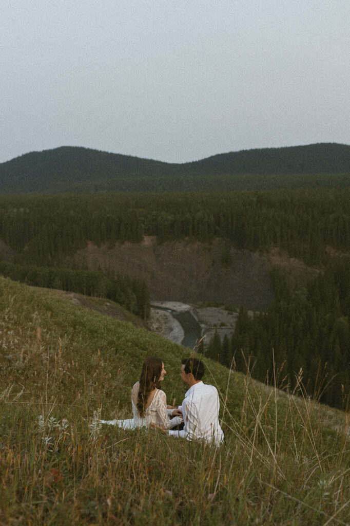 bride and groom sitting in a field together gazing upon mountain views