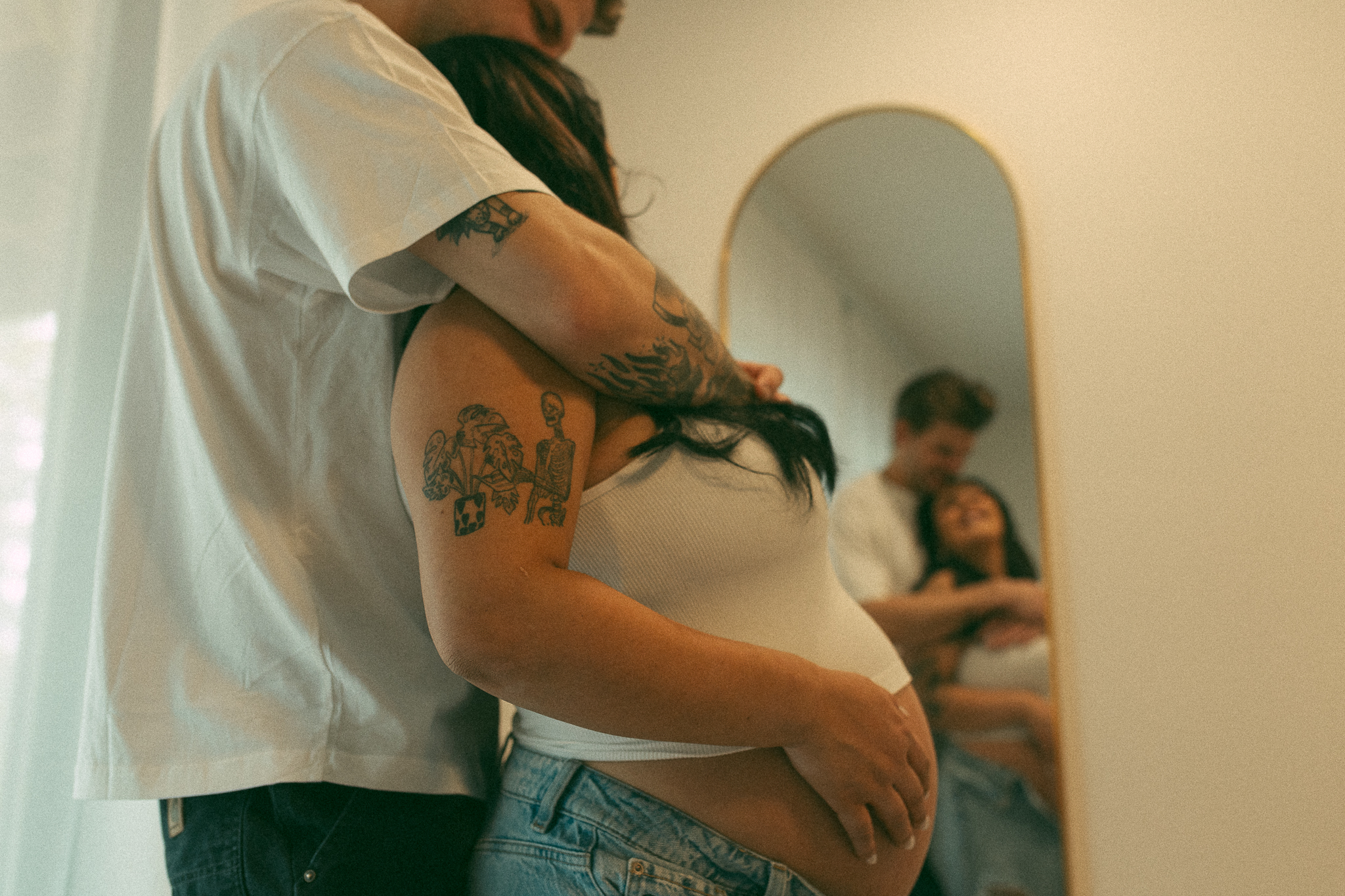 pregnant couple snuggle up with each other while looking into a mirror