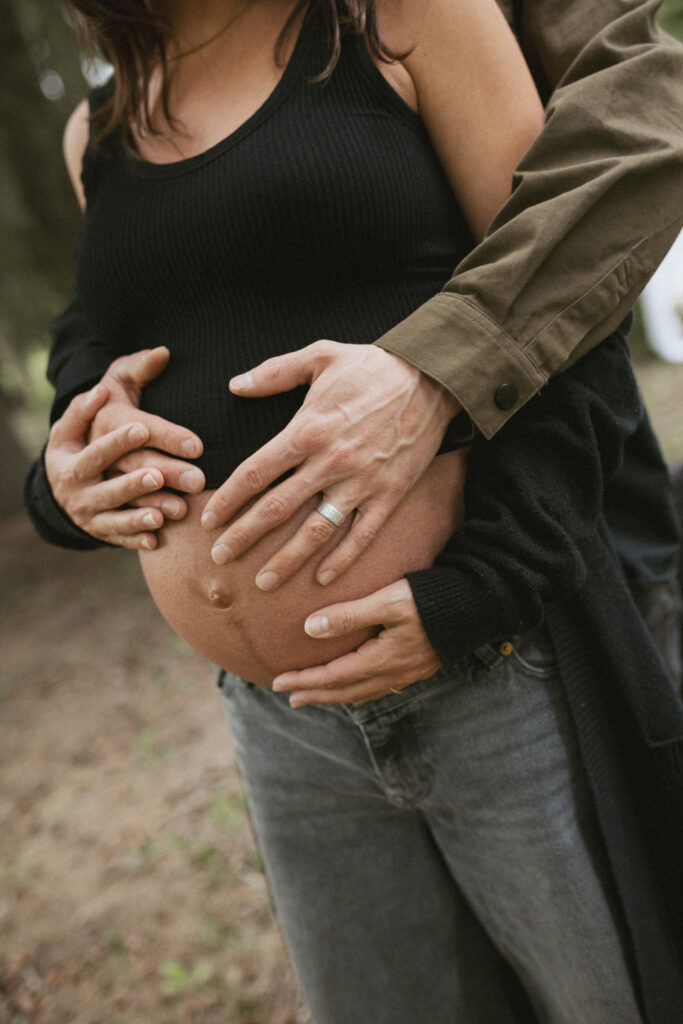 Close-up of Ang and Caleb's hands resting on her belly during their maternity session by Fernie photographer