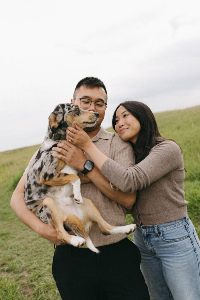 Lisa and Peter laughing together with their dog Scout at Nose Hill Park during their Calgary engagement session.